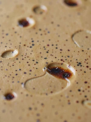 Ash-fleck speckle scattered across satin-warm stoneware glaze, faint iron blooms