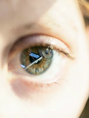 Human iris reflecting a phone screen, catch light and pupil sharp, face and devi