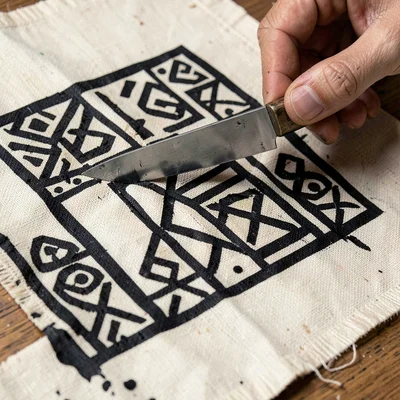 Adinkra woodblock carving detail — knife in hand cutting symbol into gourd surfa