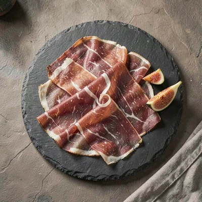 Overhead still life of a slate platter of sliced prosciutto draped in soft folds