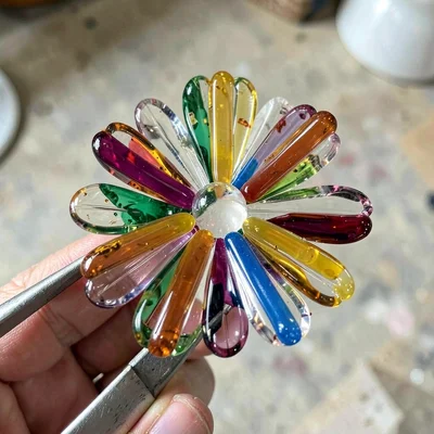Glass flower cane in tweezers — single cane held at close range showing petal la