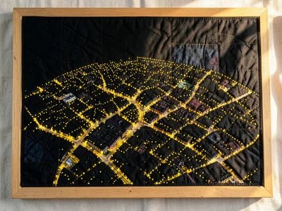 A city at night as black fabric with thousands of tiny yellow French knot lights