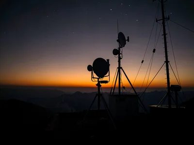 Weather station instruments silhouetted against pre-dawn gradient from orange to