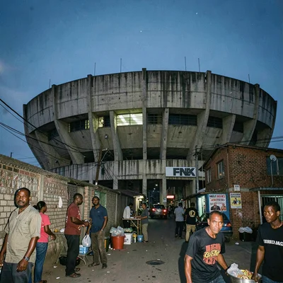 Post-industrial Johannesburg brutalism with harsh flash, FNB Stadium concrete bo