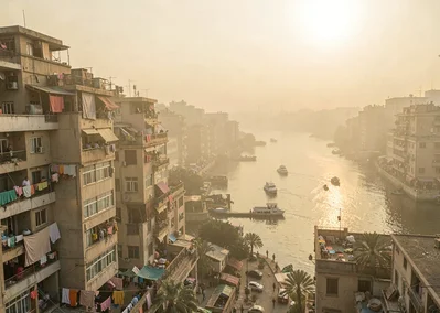 Dusty golden Cairo haze compressing apartment layers, Nile corniche at golden ho