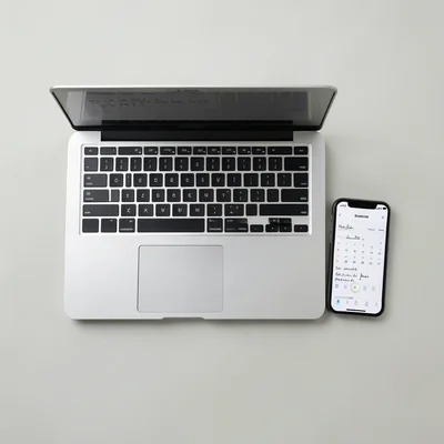 Overhead view of an open laptop, notebook with handwritten notes, phone showing 