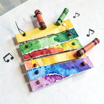 A pop-up paper xylophone with torn-paper bars and crayon mallets bouncing notes