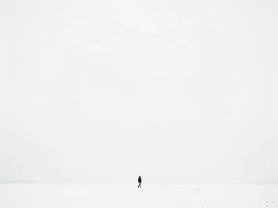 Single person at extreme bottom walking across snow field into white horizon