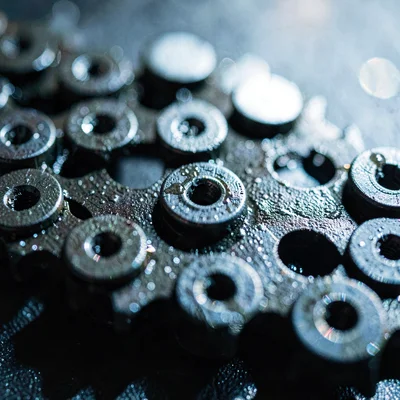 Mineral-cut macro of a chainring tooth array, oily sheen catching cool window li