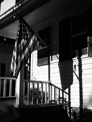 American flag on porch, dramatic shadow on white siding, patriotic noir