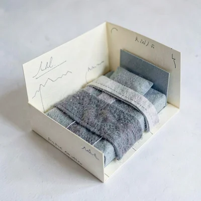 Folded-paper representation of a coastal bedroom in flat cream and grey-blue car