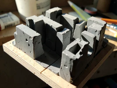 Cluster of clay megastructures squeezed onto a tilted plywood base, alleys betwe