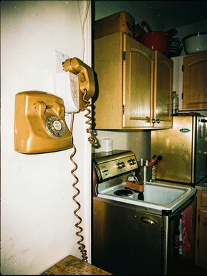 Rotary phone on kitchen wall, coiled cord stretched, harvest gold appliances bac
