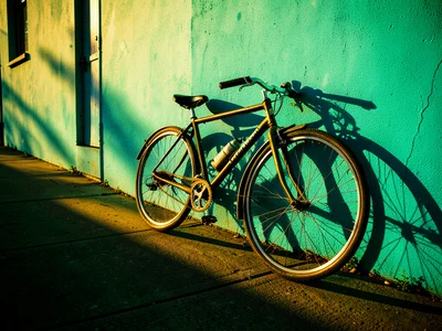 A bicycle leaning against a turquoise wall in golden afternoon light, long shado