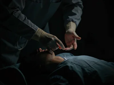 Surgeon's hands hovering above patient, gesture of intervention, life in shadow