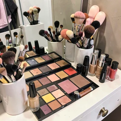 Makeup vanity covered in palettes, brushes in cups, lipsticks standing up, found