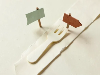A papercraft fork in a small road made of folded cream paper, two tiny matte sig