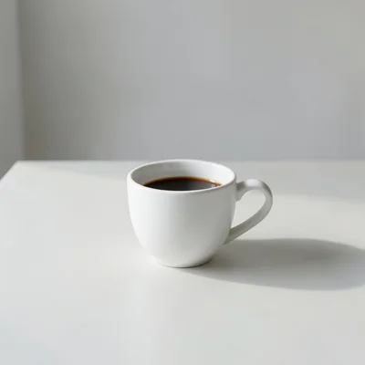 Minimalist photography of a single white coffee cup on a clean matte surface, soft natural window light, subtle shadow, 