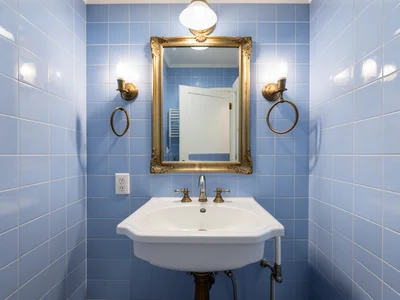 Bathroom in powder blue tile, symmetrical mirrors, centered sink, vintage fixtur