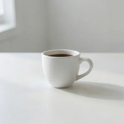 Minimalist photography of a single white coffee cup on a clean matte surface, soft natural window light, subtle shadow, 