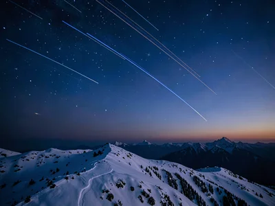 Star trails visible in deepening blue above a snow ridge at twilight
