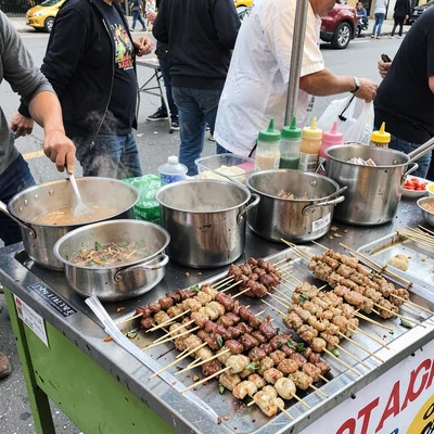 Street food cart with multiple pots bubbling, skewers arranged in rows, condimen
