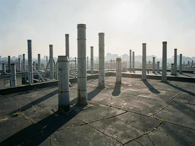 Midday haze glares above a dense vent stack field, casting short stubby shadows 