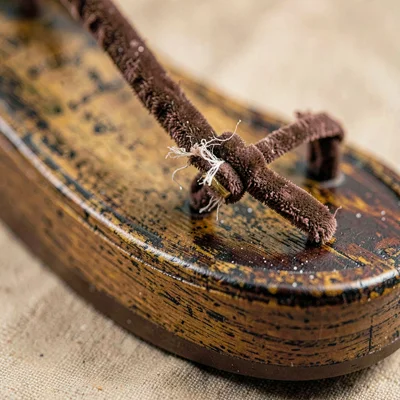 Mineral-cut detail of a wooden geta sandal with worn lacquer and frayed velvet t