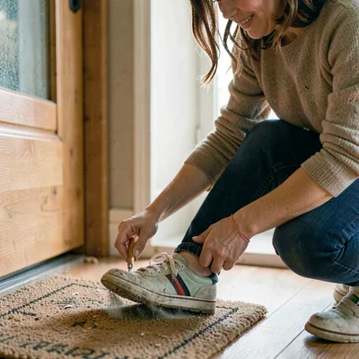 Side-light portrait of a parent dusting off a child's shoe by a doormat
