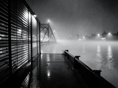Bridge at night with fog rolling across, distant city lights hazy through mist