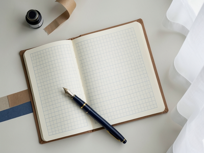 Overhead flat-lay photograph of Japanese stationery on a desk surface,. A calm, minimal desk scene featuring a Japanese 