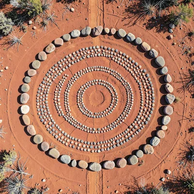 Dry creek bed stones arranged in concentric rings on red earth, flat-lay