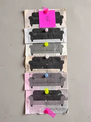 Stacked newsprint cutouts of identical sofa silhouettes pinned in a tight column
