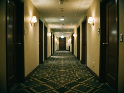 A hotel hallway with geometric carpet, repeating doors stretching to a vanishing