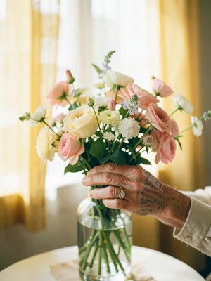 Elderly hands arranging flowers in the same vase they've used for forty years, s