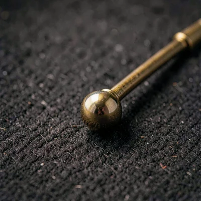 Macro 2:3 of a polished pendulum bob and rod against dark felt