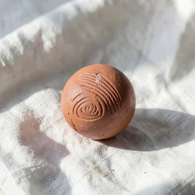Bared terracotta plum pit with thumb-pressed grooves along its surface, on plain