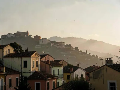 Distant ridge town backlit at late afternoon, walls in silhouette against a pale