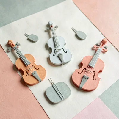Papercraft composition of layered paper-cut musical instruments across cream pap