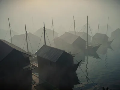 Fishing village rooftops emerging from sea fog with mast tips of moored boats po