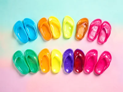 Knolled rainbow of jelly sandals lined up by color from cyan to magenta across a