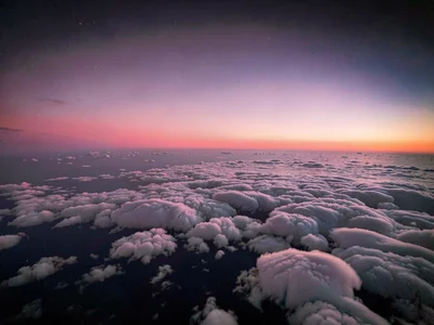 Thin clouds at high altitude catching sunrise pink against already-dark upper at