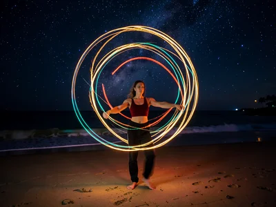 Fire dancer's poi creating orbital patterns, long exposure, beach at night, star