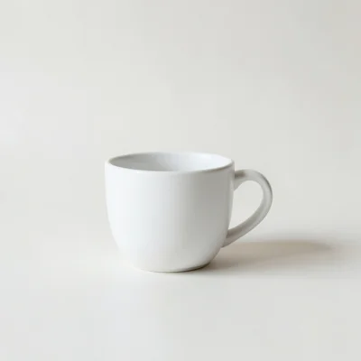 Minimalist studio photograph of a single white coffee cup on a clean matte surface, centered composition, soft diffused 