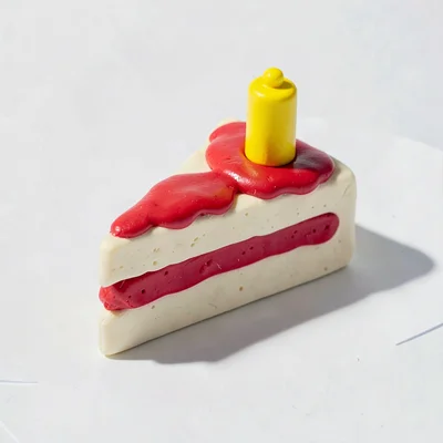 Quirky chunky clay slice of birthday cake in cream-white with cherry-red chunky