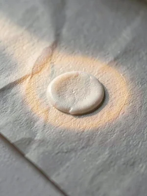 Glue-spot raised mound on parchment catching directional light with warm fiber h