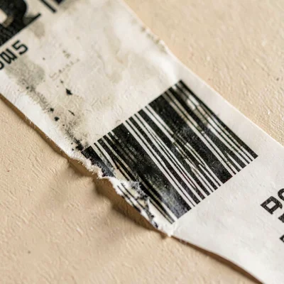 Surface macro of a stamped barcode label peeling at one corner, ink bleed