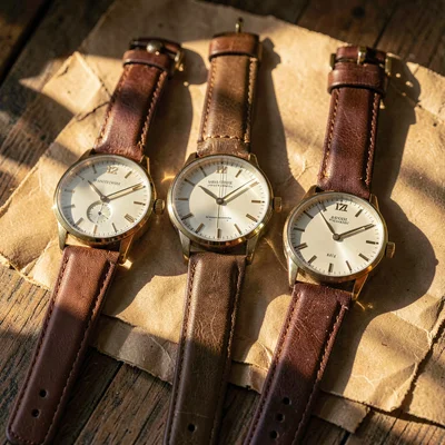 Warmstack arrangement of three wristwatches on aged kraft paper, leather straps 