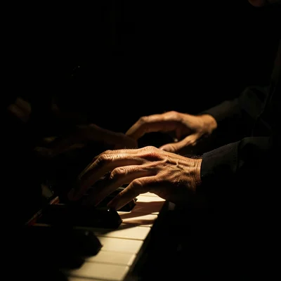 A pianist's hands on ivory keys, a single overhead spot creating dramatic shadow