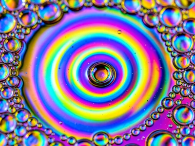 Motor oil dropped on puddle water, rainbow film spreading outward in concentric 